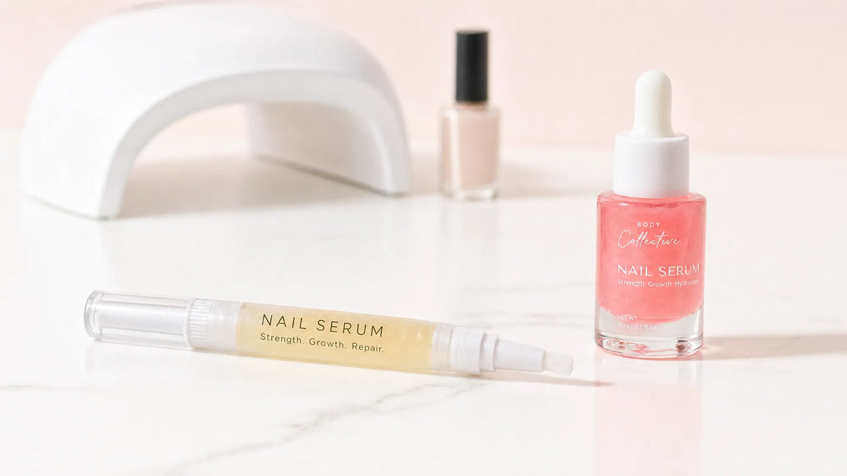 A Body Collective nail serum pen and 15 ml dropper on a marble bench in front of a UV lamp and a blank polish bottle