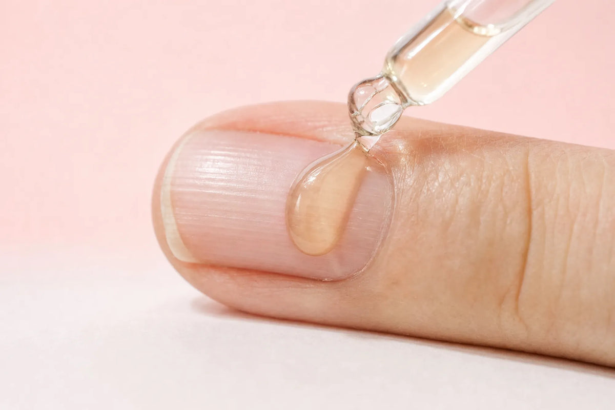 A drop of nail serum from the dropper on a natural nail with light vertical ridges