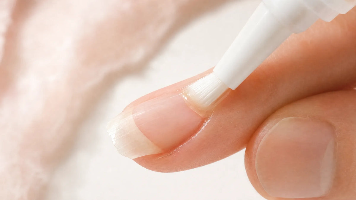 Brushing nail serum onto a nail that is peeling at the edge